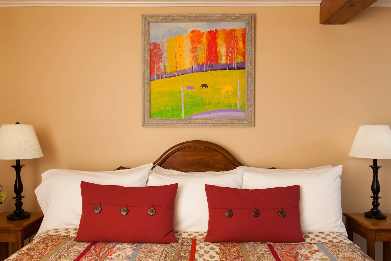 What to Know About the Mount Washington Hike 2 Stay at our New Hampshire Bed and Breakfast. Here is a king sized bed with red pillows and colorful artwork hanging over the bed.