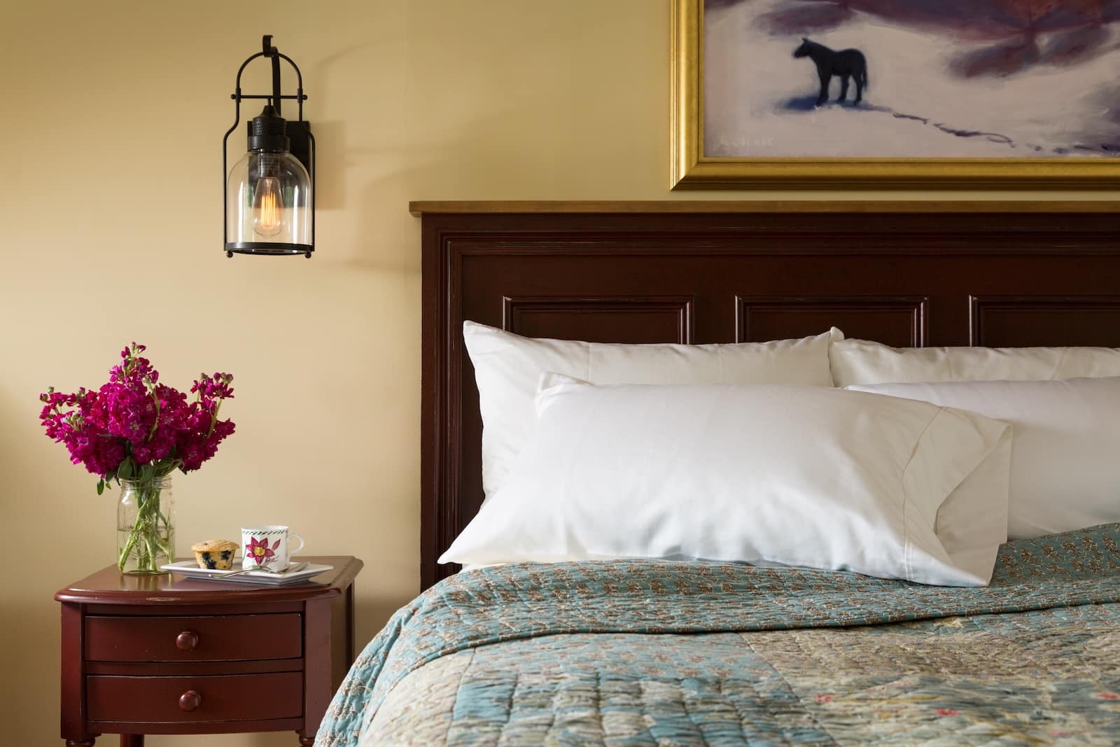 Stay at one of the best New Hampshire Inns during your visit to the White Mountains. An image of a bed with flowers on the bedside table. 