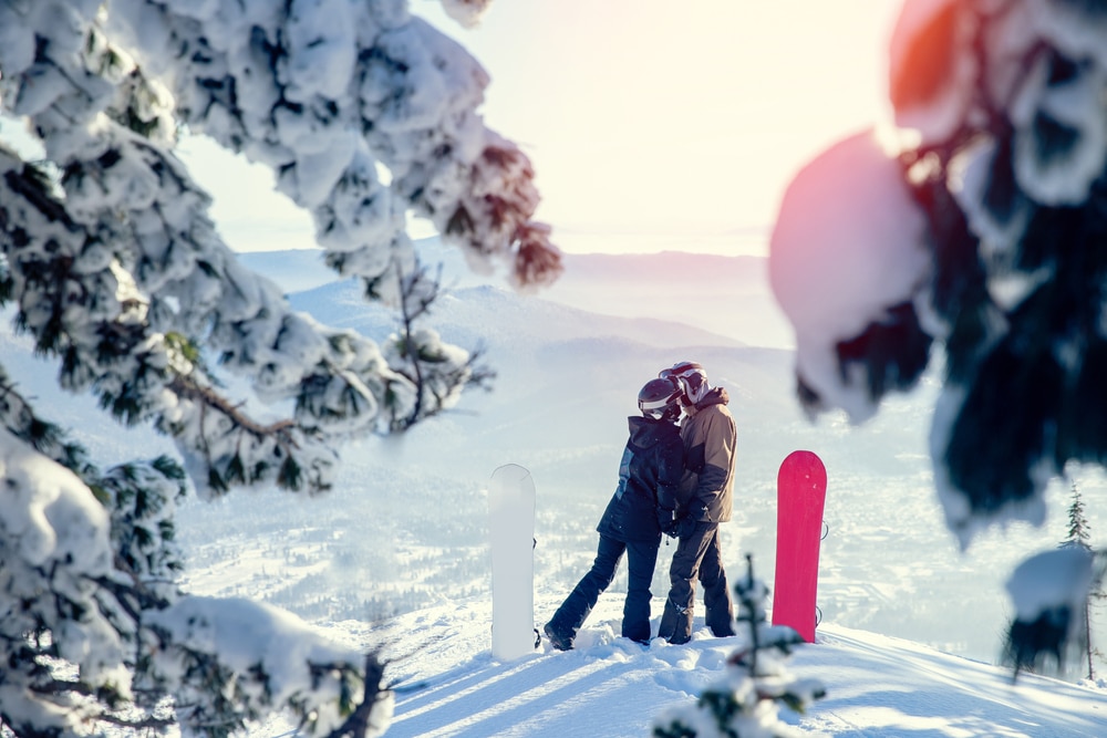 A couple sneaks a kiss while snowboarding at Bretton Woods skiing area and other top-rated New Hampshire Ski Resorts