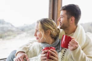 A young couple snuggles up with cups of coffee on their romantic getaway in New Hampshire.