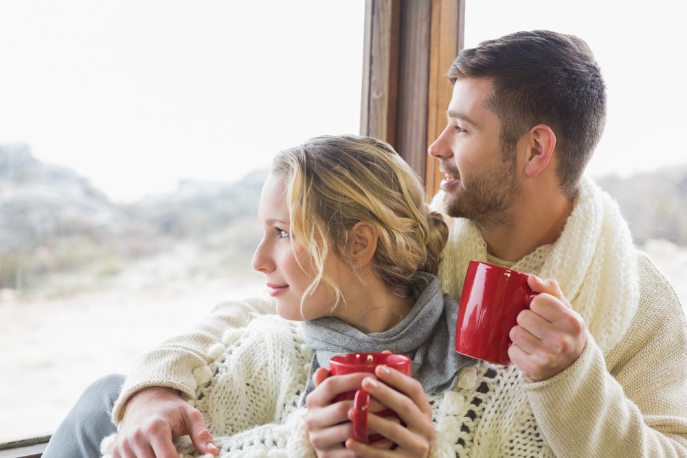 A young couple snuggles up with cups of coffee on their romantic getaway in New Hampshire.