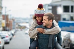 A smiling man gives a piggy back ride to his female companion on a romantic winter getaway to one of the best New Hampshire Inns.